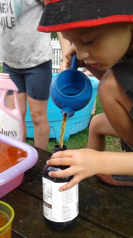 A child carefully pouring water from a watering can into a bottle