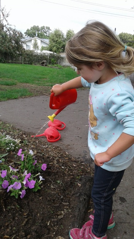 A girl watering the garden with a red watering can